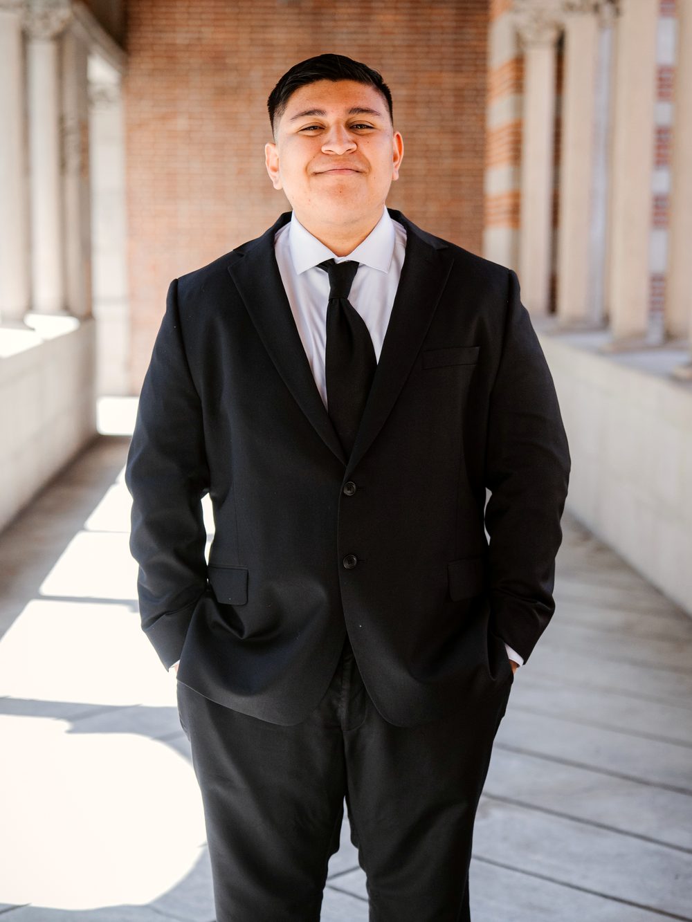 Nathan Castillo in a dark suit, photographed in a campus colonnade
